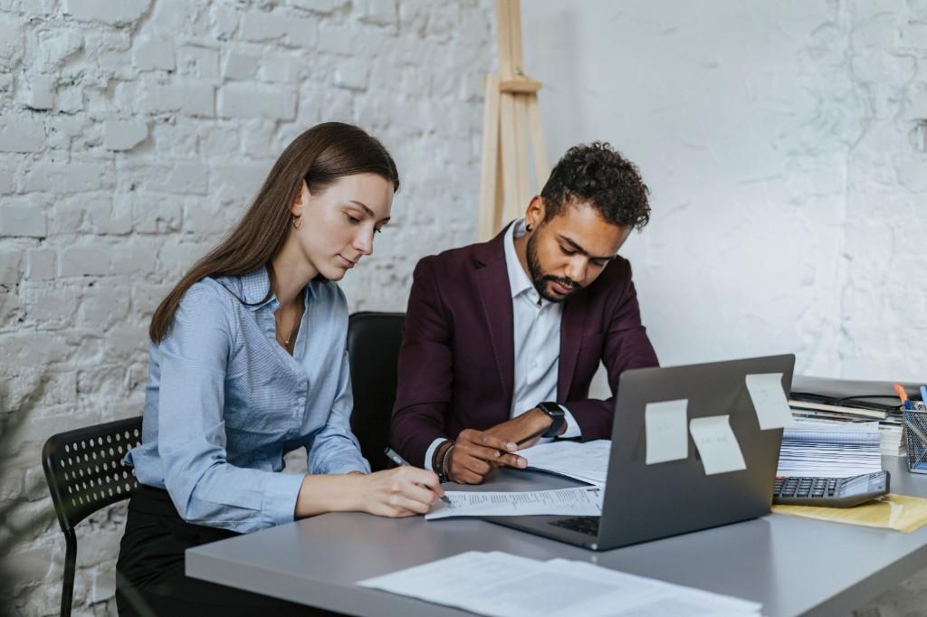 Two professionals collaborating at a desk while reviewing and signing documents